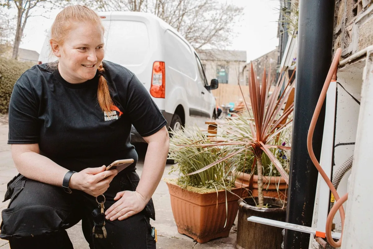 Fay Dolphin of Dolphin Heating checking a boiler flue outside a house, her van behind her